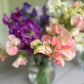 Bouquets of pink and purple sweet pea flowers in clear vases on a wooden surface.