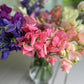 Bouquet of colourful sweet pea flowers in a clear vase on a wooden surface